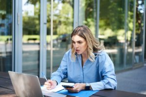 Kobieta siedzi przy stole z laptopem i telefonem komórkowym, przeglądając Internet.