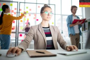 Kobieta siedząca przy biurku przed niemiecką flagą, trzymająca się niemieckich standardów projektowania stron internetowych.